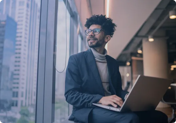 Homem sorrindo usando notebook perto de uma janela
