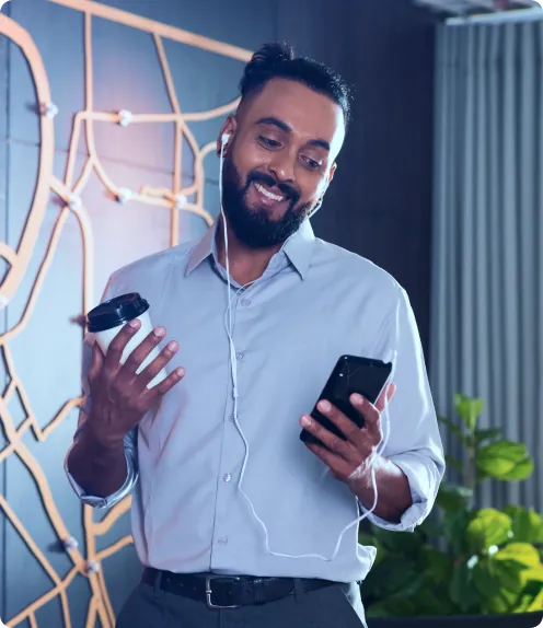 Homem sorrindo olhando o celular e segurando um café